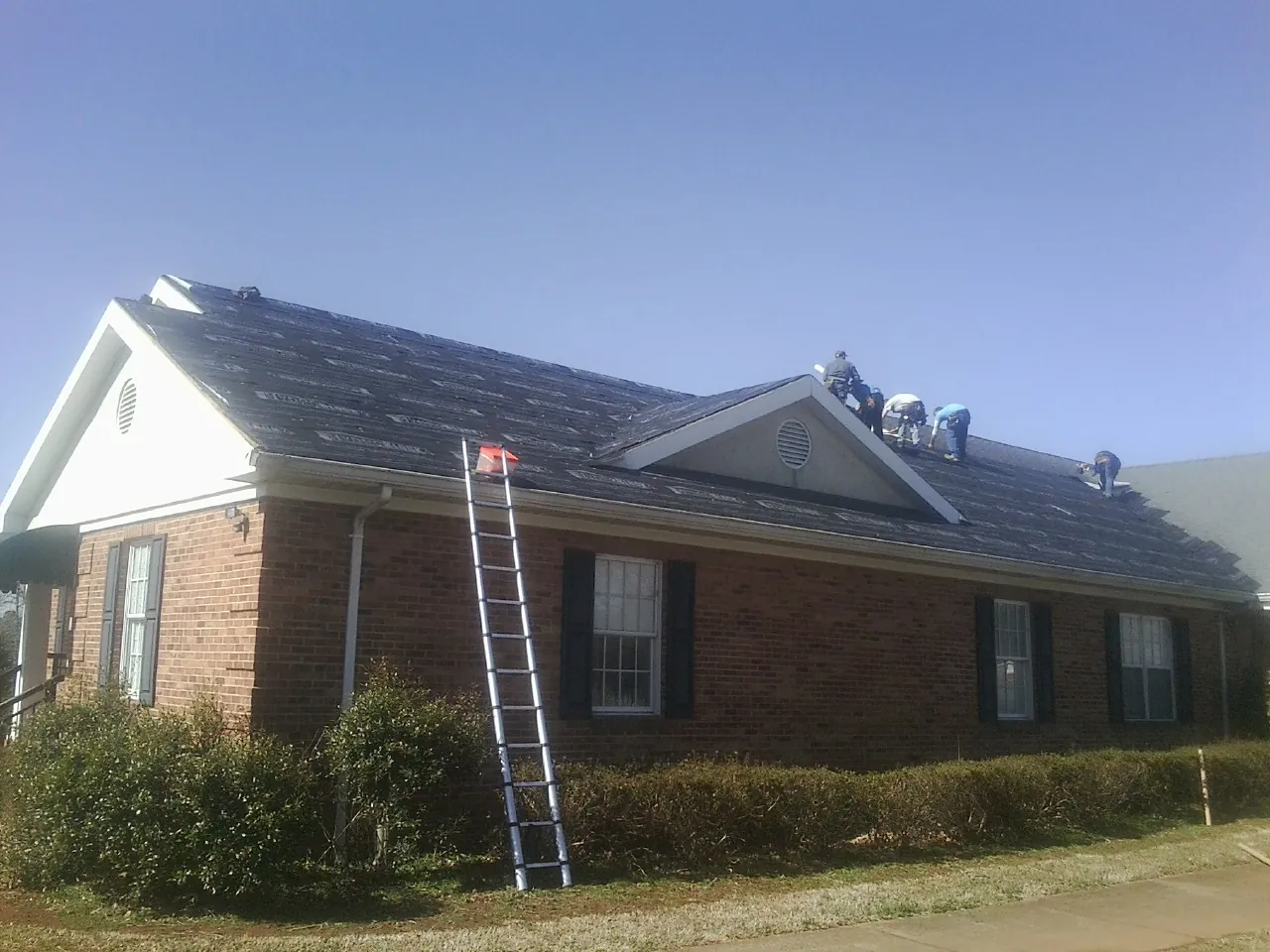 Crew tearing shingles off a brick ranch roof with a ladder set — Metal Roof Repair work by our crew in Higganum