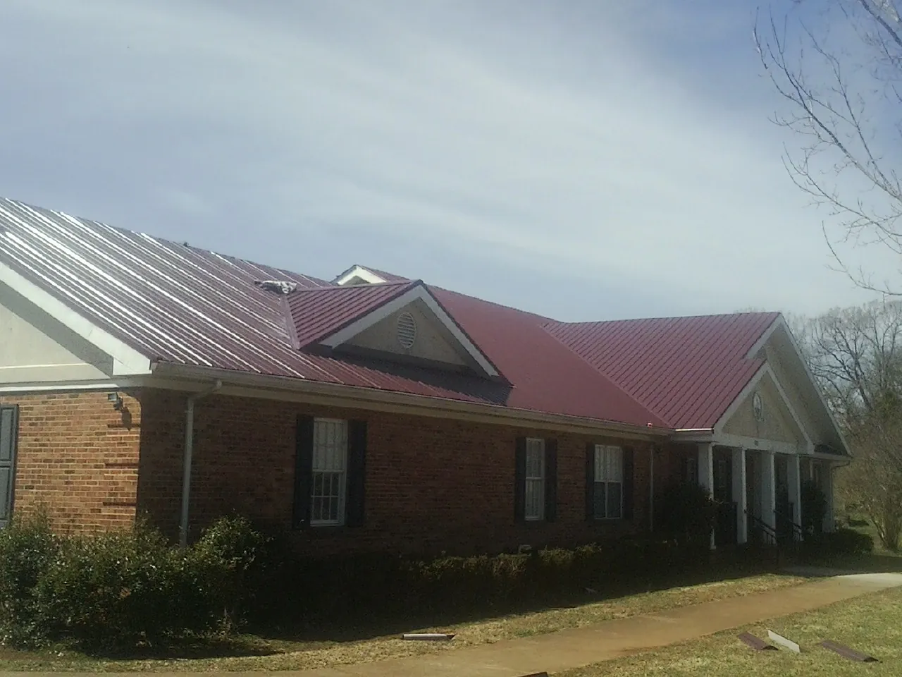 Red metal roof with gabled entries on a long brick building, from a Hail Damage Roof Repair job in Higganum