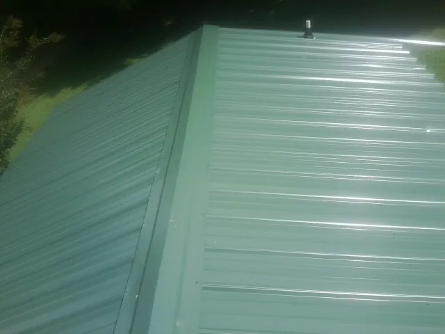 New green metal panels meeting at the ridge of a roof — Flat Roof Repair work by our crew in Higganum
