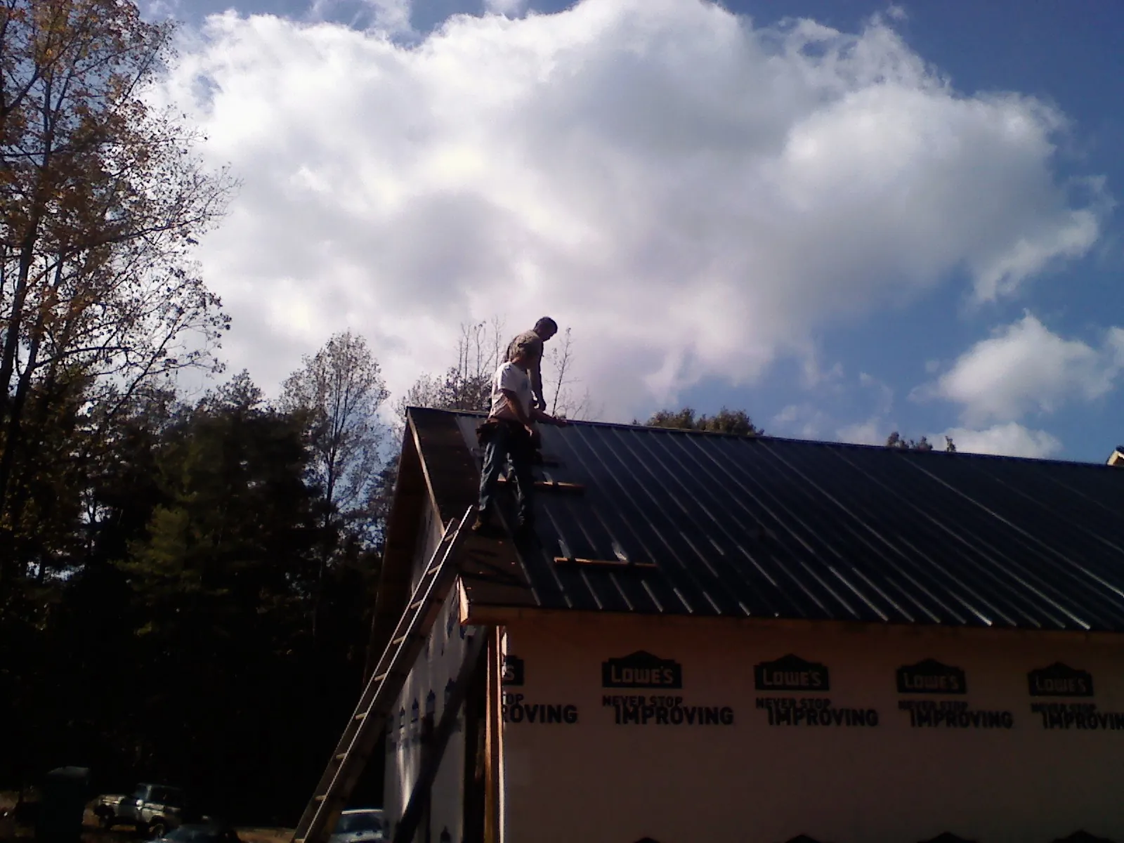 Roofer fastening dark metal panels high against a cloudy sky, from a Roof Inspection job in Higganum
