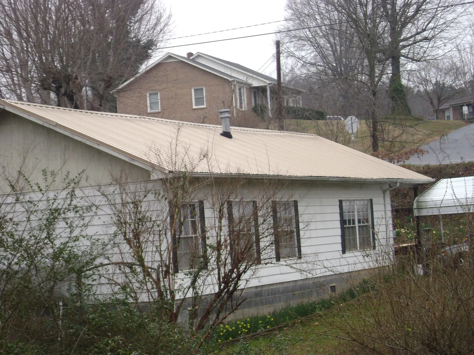 Tan metal roof on a white sided house set into a hillside — Commercial Roofing by Roofing Brothers in Higganum